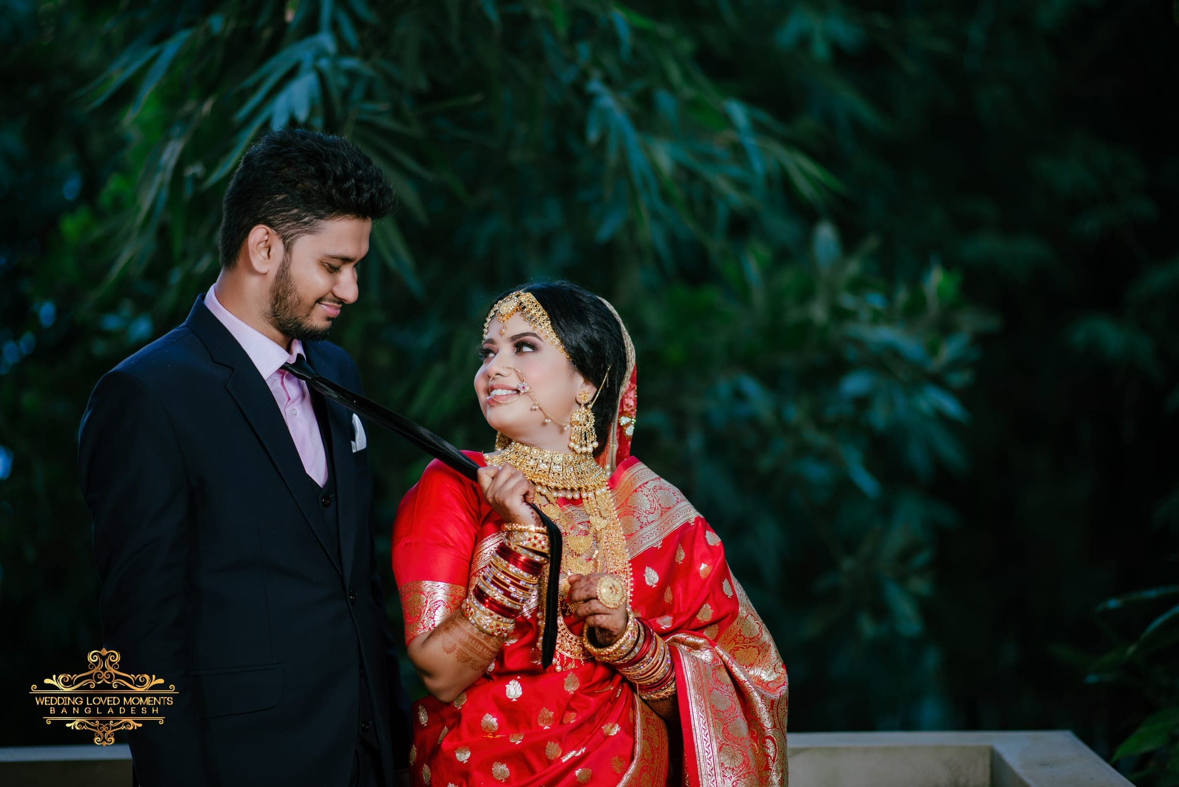 Couple sharing a smile in a garden, the bride in a red Banarasi saree and the groom in a navy suit