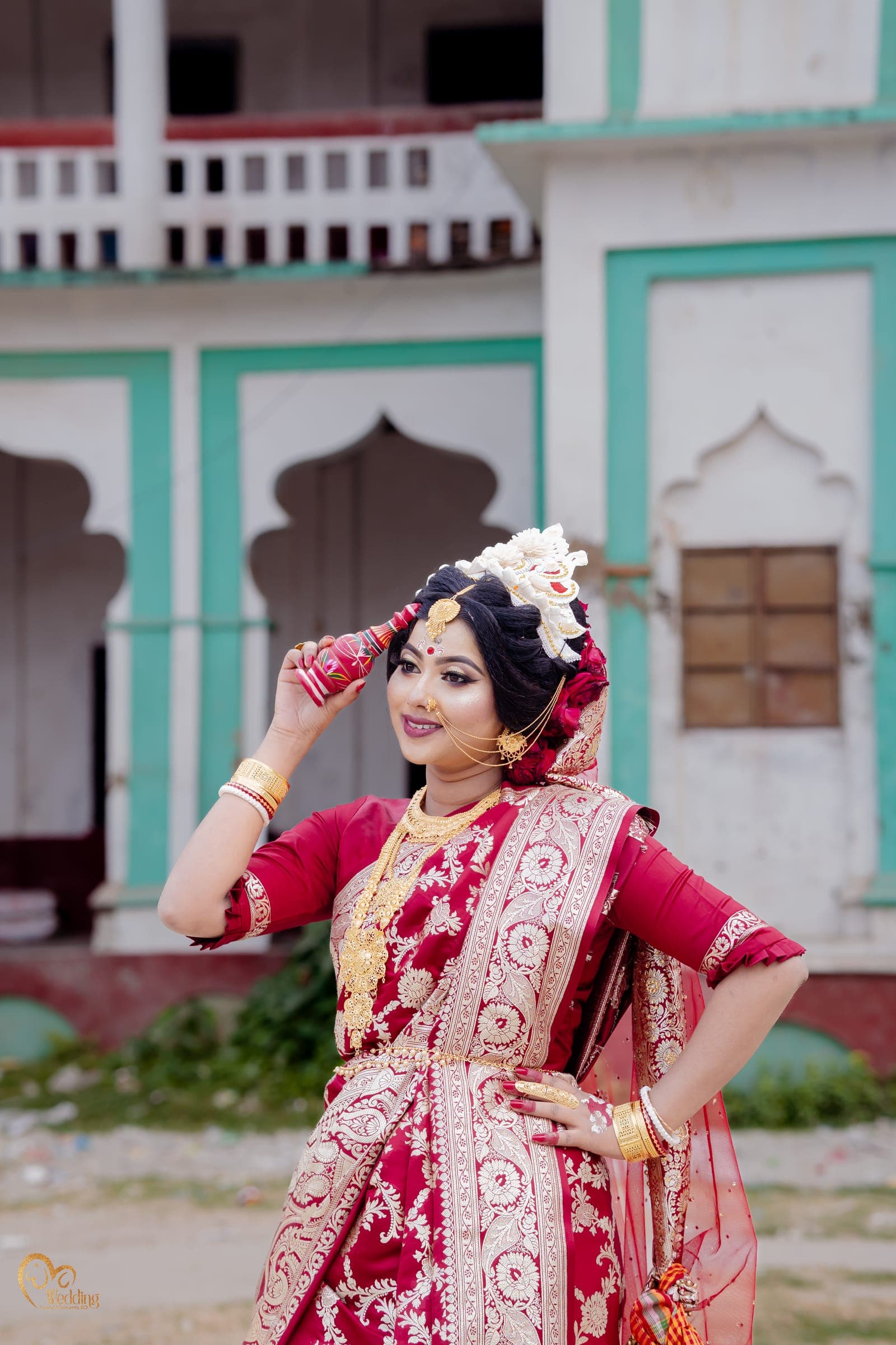 Bride in a red and white saree posing playfully in front of a heritage building