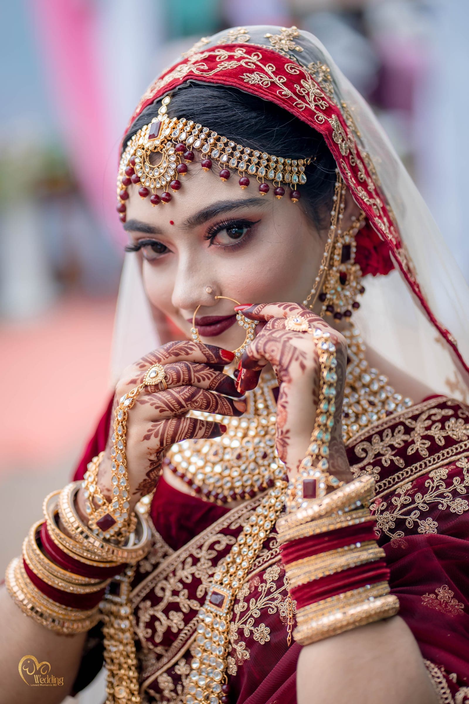 Bride in red framing her face with henna-decorated hands and gold bangles