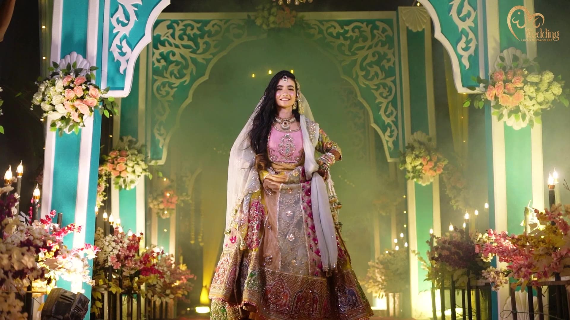 Bride in a pastel lehenga before a carved floral stage