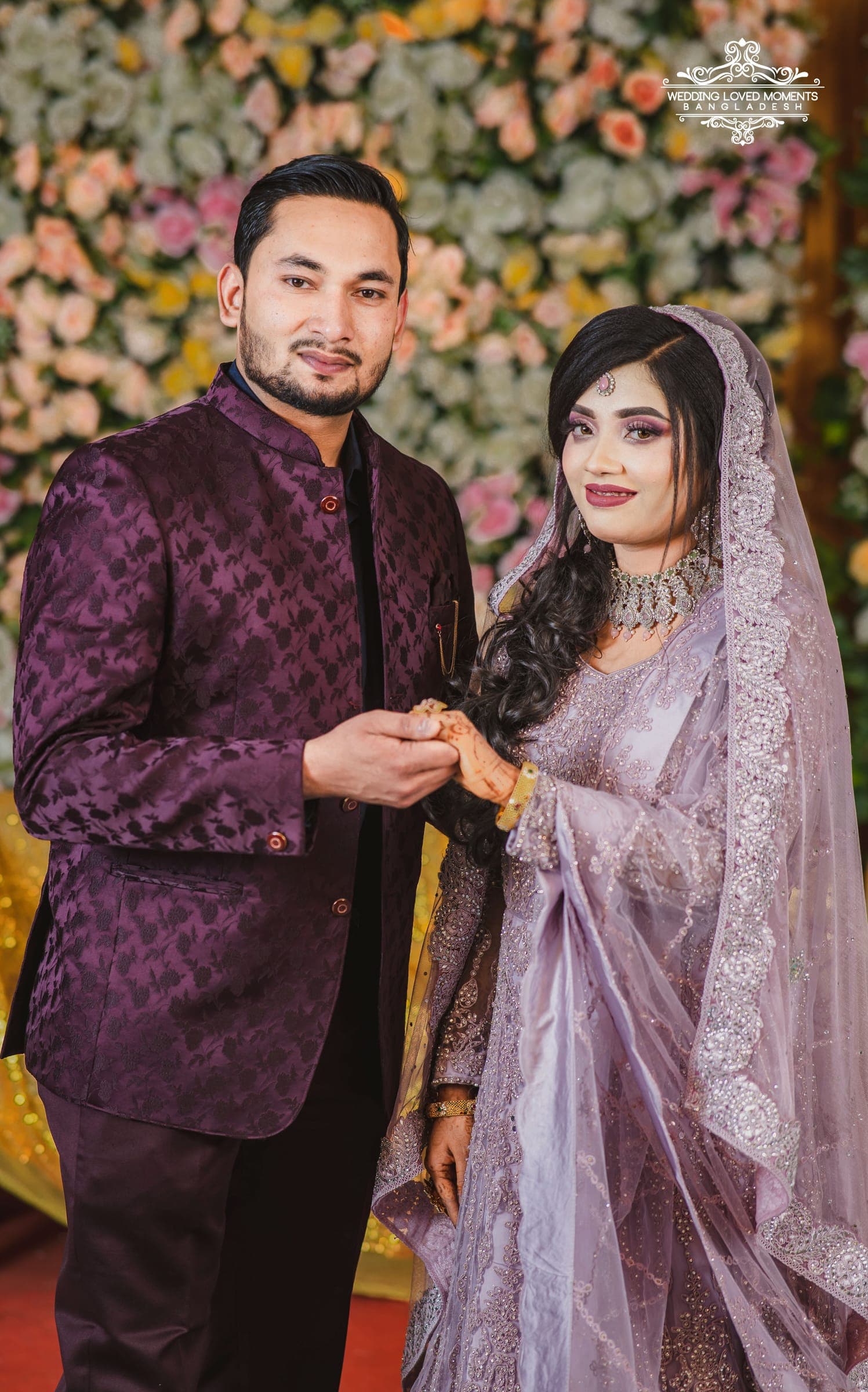 Groom placing a ring on the bride's finger in front of a floral stage